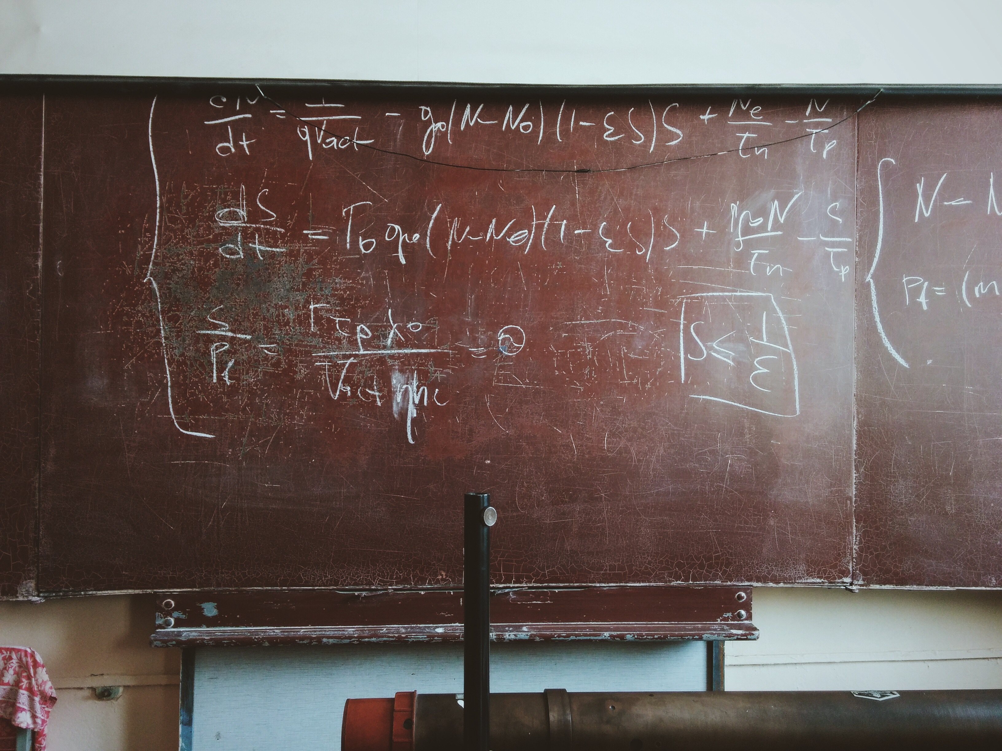 Brown board in a classroom, with writings in chalk on it