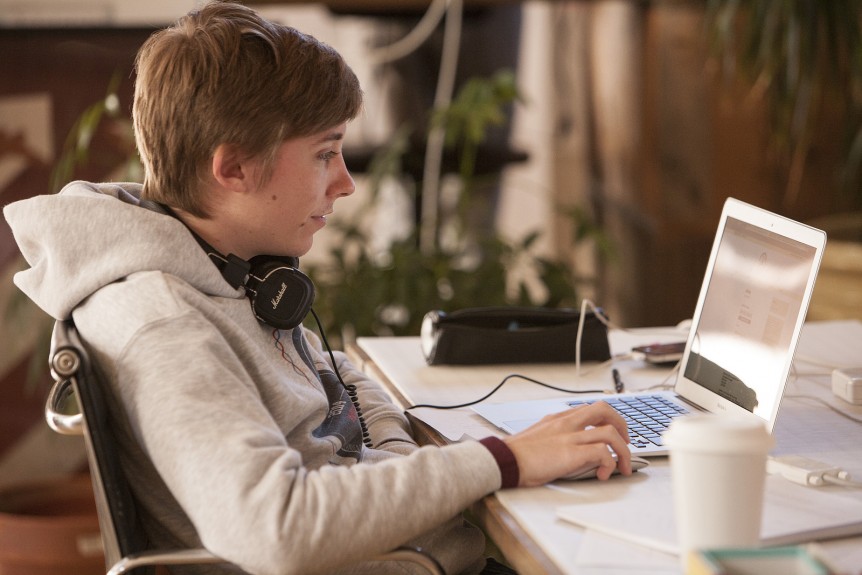 A person working on a laptop, with headphones around their neck