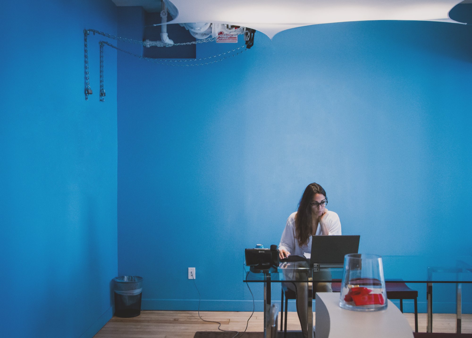 Woman working on a laptop placed on a desk, in a room whose walls are painted blue