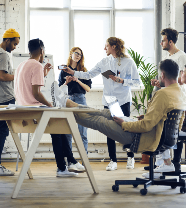 Colleagues, some seated and some standing around a table, discussing in front of a whiteboard