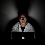 A man sitting in front of a laptop, with light glaring from its screen