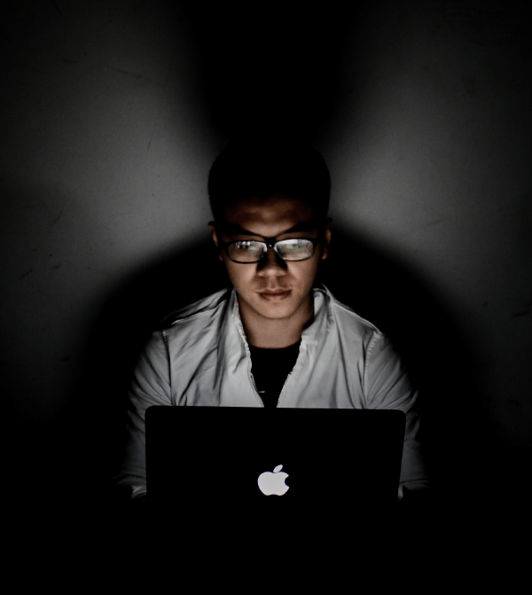 A man sitting in front of a laptop, with light glaring from its screen