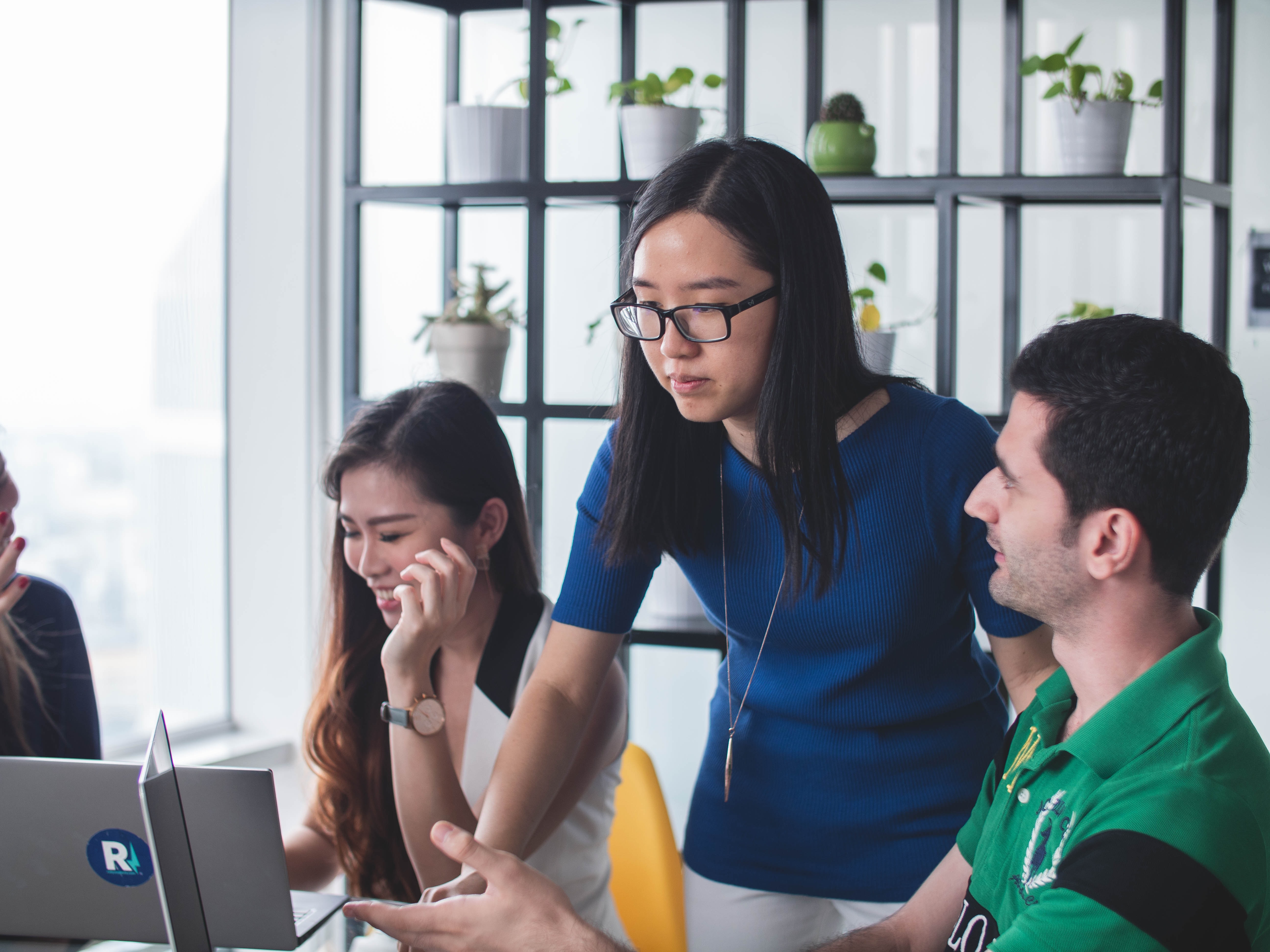 A woman looking at a computer screen, with a man on her right explaining something to her and a smiling woman seated on the left