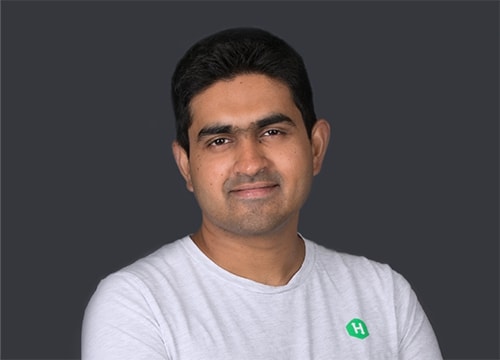 Vivek Ravisankar is smiling into the camera, wearing a white HackerRank t-shirt against a dark grey background.